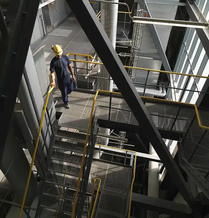 A man ascends a staircase within a factory, showcasing the industrial environment and his purposeful moveme